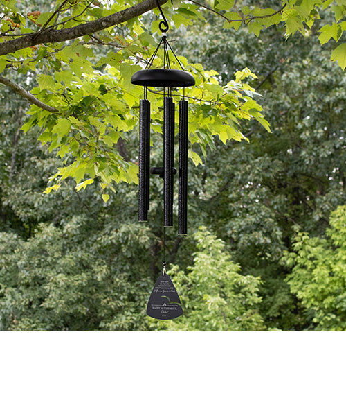 Black wind chime hanging from a tree with green leaves in the background
