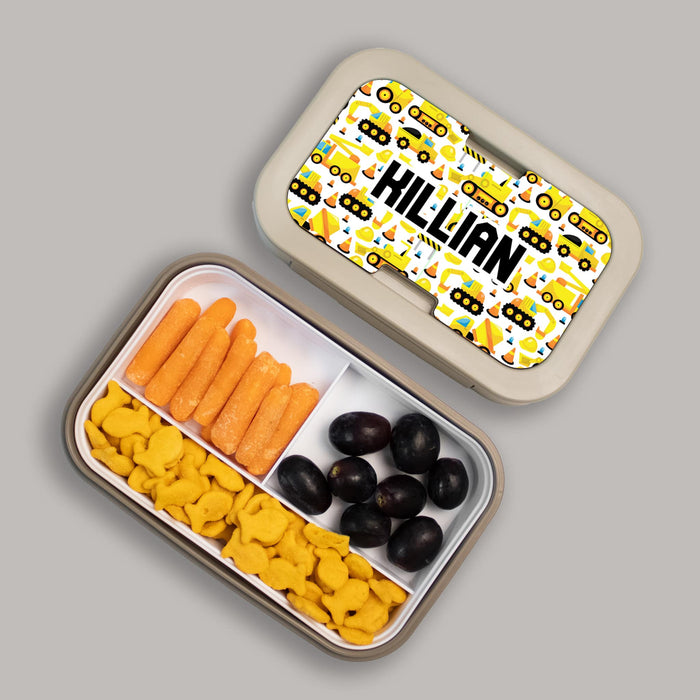 Bento box with a construction vehicle design and compartments of snacks on a gray background