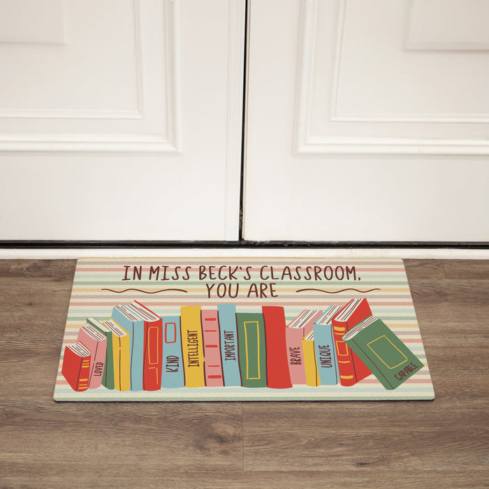 Personalized classroom doormat with colorful books design and text on a wooden floor.
