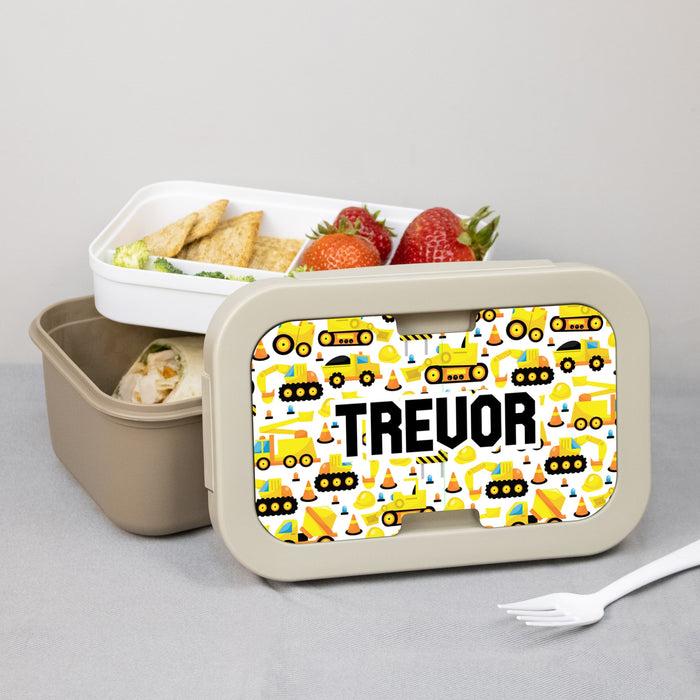 Lunch box personalized with name on a construction vehicle pattern, containing snacks and a fork.
