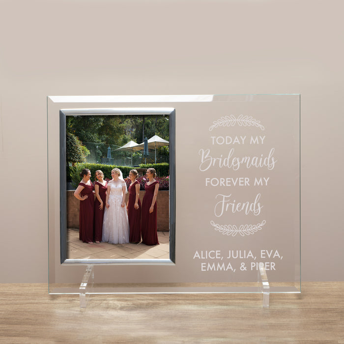 Glass frame with a photo of a bride and bridesmaids, engraved text, on a beige wall.