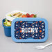 Blue lunch box with sports pattern and  name, containing a meal and a fork on a gray background.