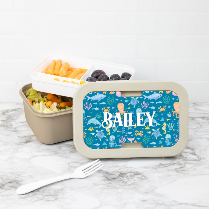 Personalized lunch box with a blue sea-themed design, containing snacks on a marble surface.