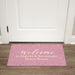 Pink dorm room doormat with floral designs and text on a wooden floor.