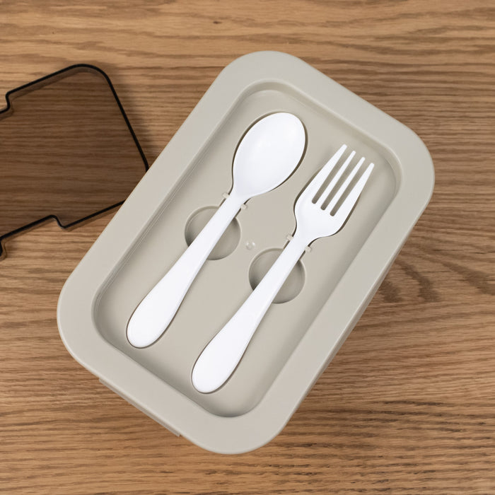 Spoon and fork set in a beige lunch box on a wooden surface
