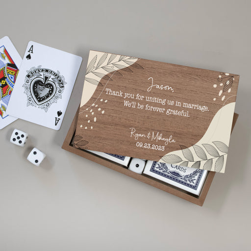 Personalized playing card set with wedding officiant thank you on a wooden box, surrounded by playing cards and dice.