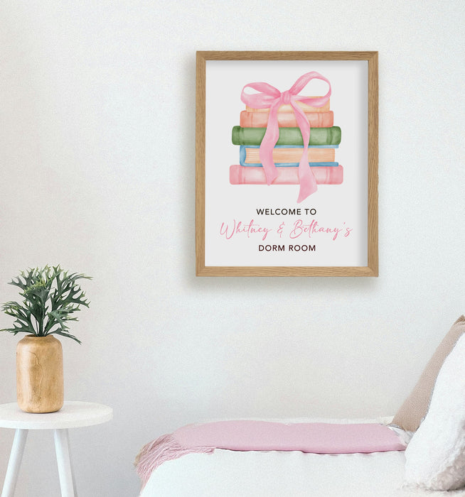 Framed artwork with books and a bow on a wall in a dorm room setting.