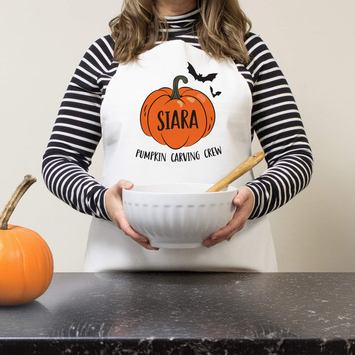Person wearing a Halloween-themed apron with a pumpkin design and text, holding a bowl.