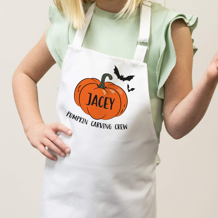 Child wearing a white apron with a pumpkin design and halloween text, on a plain background