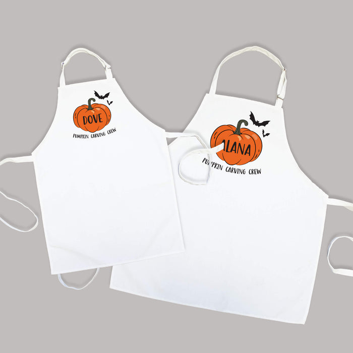 Two white aprons with pumpkin designs and names on a gray background
