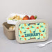 Lunch box with dinosaur pattern and 'ZACHARY' text, containing snacks on a gray background