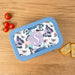 Butterfly-patterned lunch container with a blue rim on a wooden surface with tomatoes and crackers.
