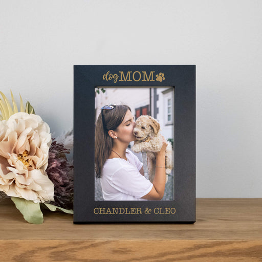 Personalized photo frame with 'dog MOM' text, holding a photo of a woman and dog, on a wooden surface with flowers.