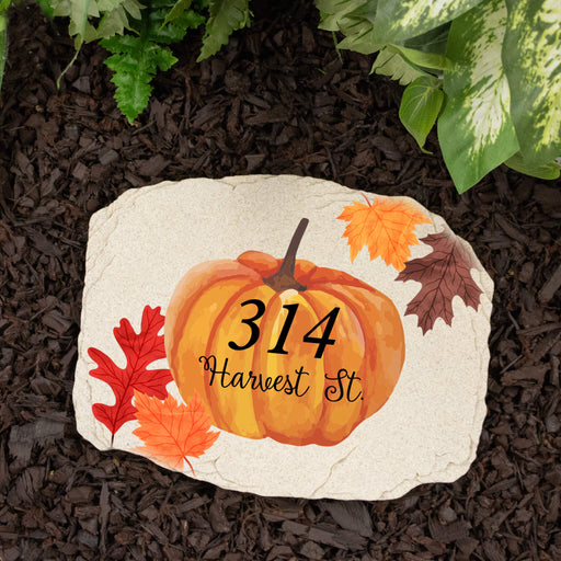 Decorative garden stone with pumpkin design and home address on a mulched surface