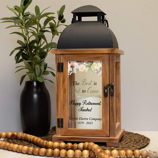Wooden retirement gift lantern with printed message next to a plant and beads on a neutral background
