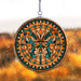 Decorative circular stained glass inspired acrylic suncatcher with orange and blue butterfly design, hanging against a rain covered window blurred background