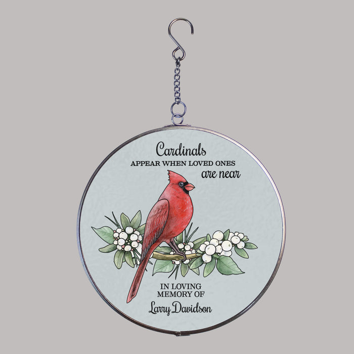 round acrylic suncatcher with a red cardinal sitting on a tree branch design in front of a gray background