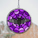 Stained glass suncatcher with a bat and spider web design hanging against a window