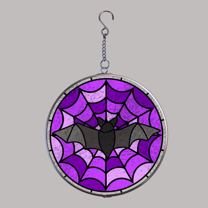 Round stained glass suncatcher with purple spider web and black bat design on a gray background