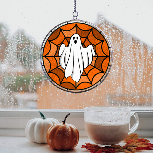 Halloween-themed suncatcher window hanging with pumpkins and a mug on a windowsill.